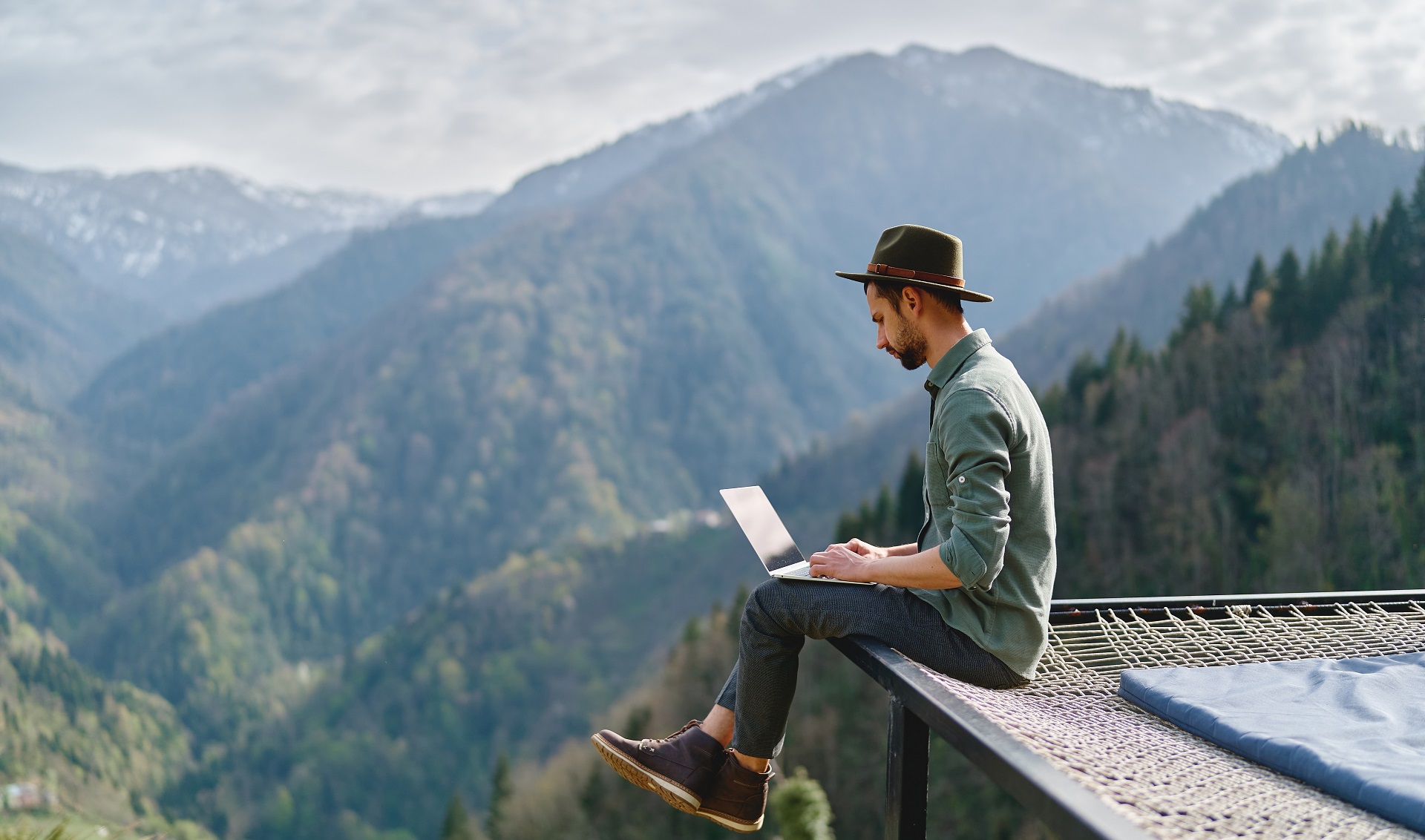 Ein Mann sitzt vor einer Berglandschaft an einem Laptop