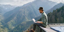 Ein Mann sitzt vor einer Berglandschaft an einem Laptop