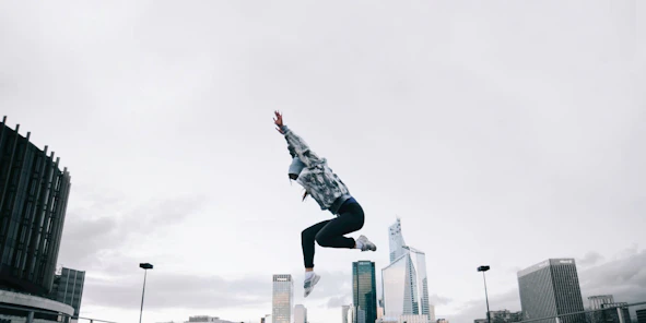 Ein Mensch springt hoch auf einer Autobahnbrücke, im Hintergrund ist die Skyline einer Stadt zu sehen