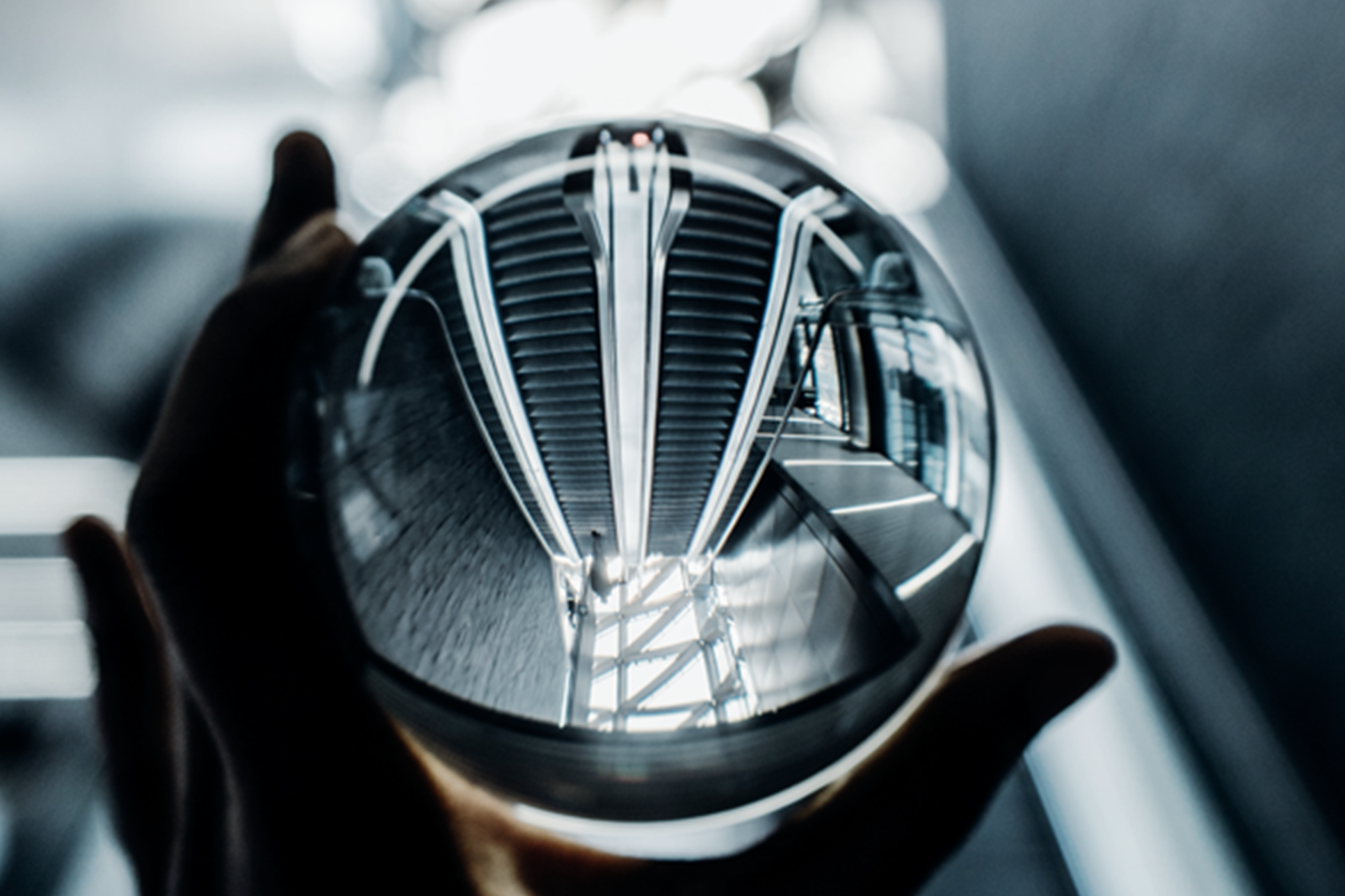 Eine Hand hält eine Glaskugel in der sich ein Treppenaufgang spiegelt