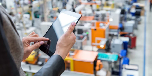 Eine Hand hält ein Tablet vor unscharfem Fabrik-Hintergrund
