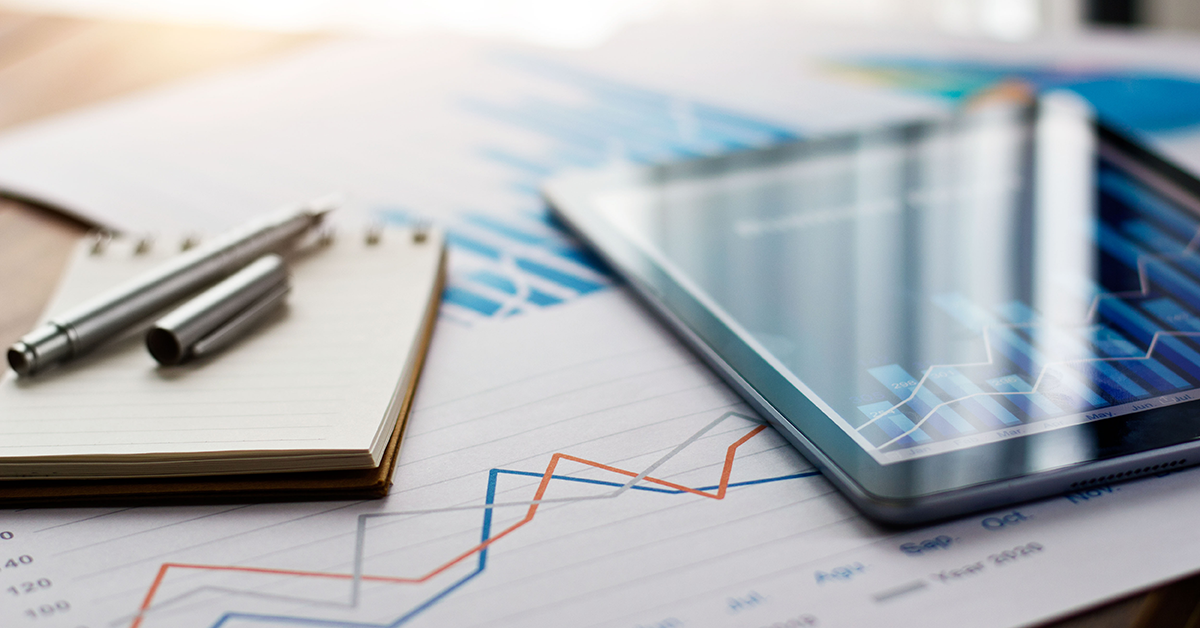 Ein Notizblock mit Stift, ein Tablet und bedruckte Blätter liegen nebeneinander