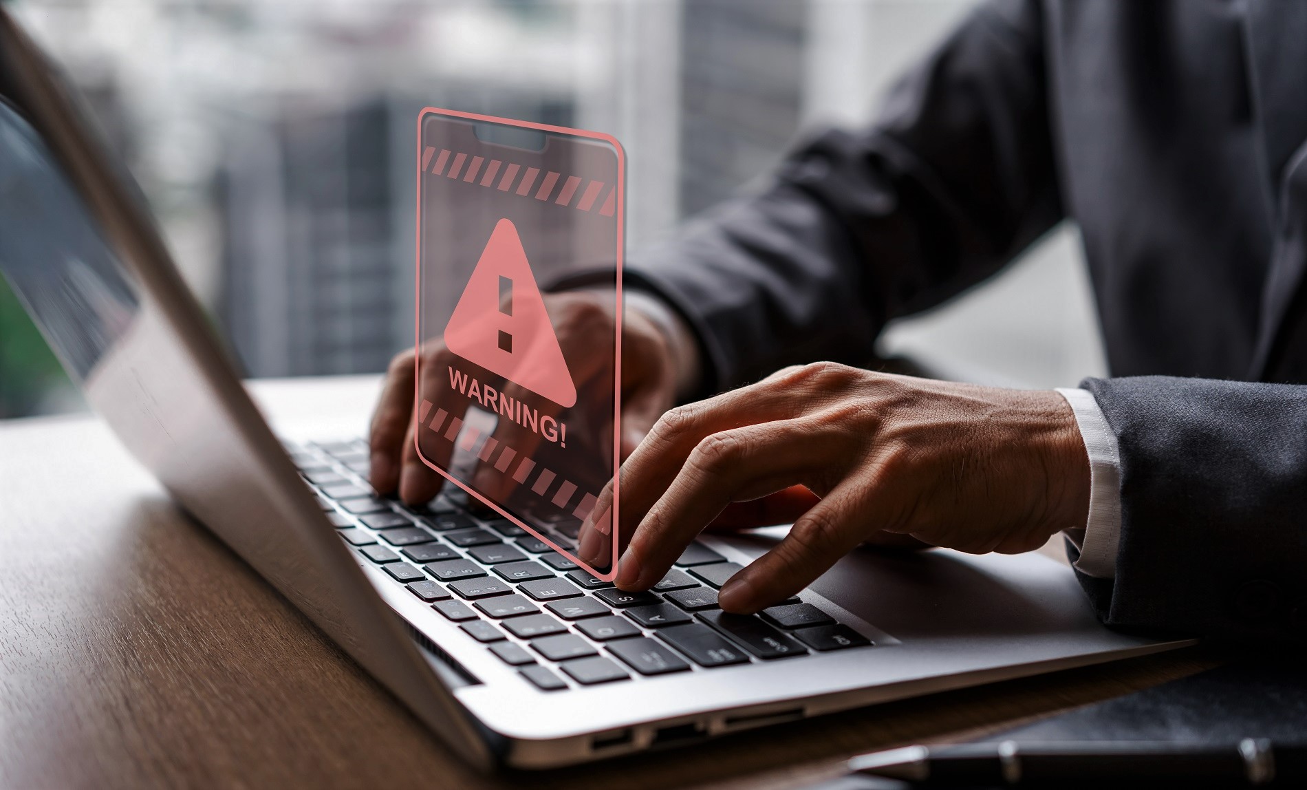 Hände tippen auf einem Laptop, darüber ein Warndreieck