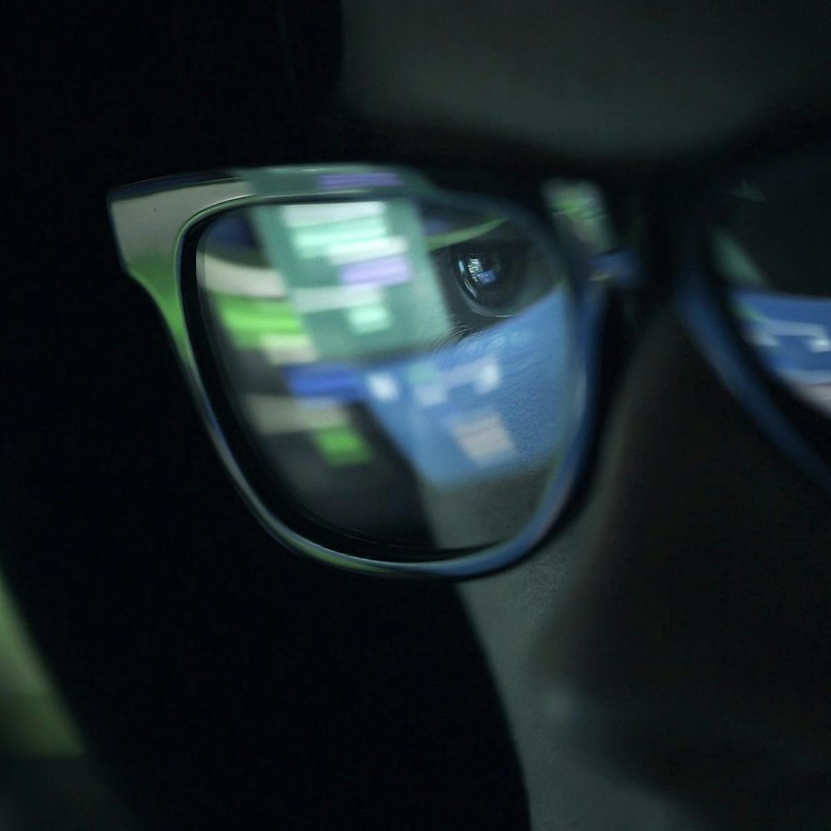 Person mit Kapuze und Brille, in der sich ein Bildschirm spiegelt