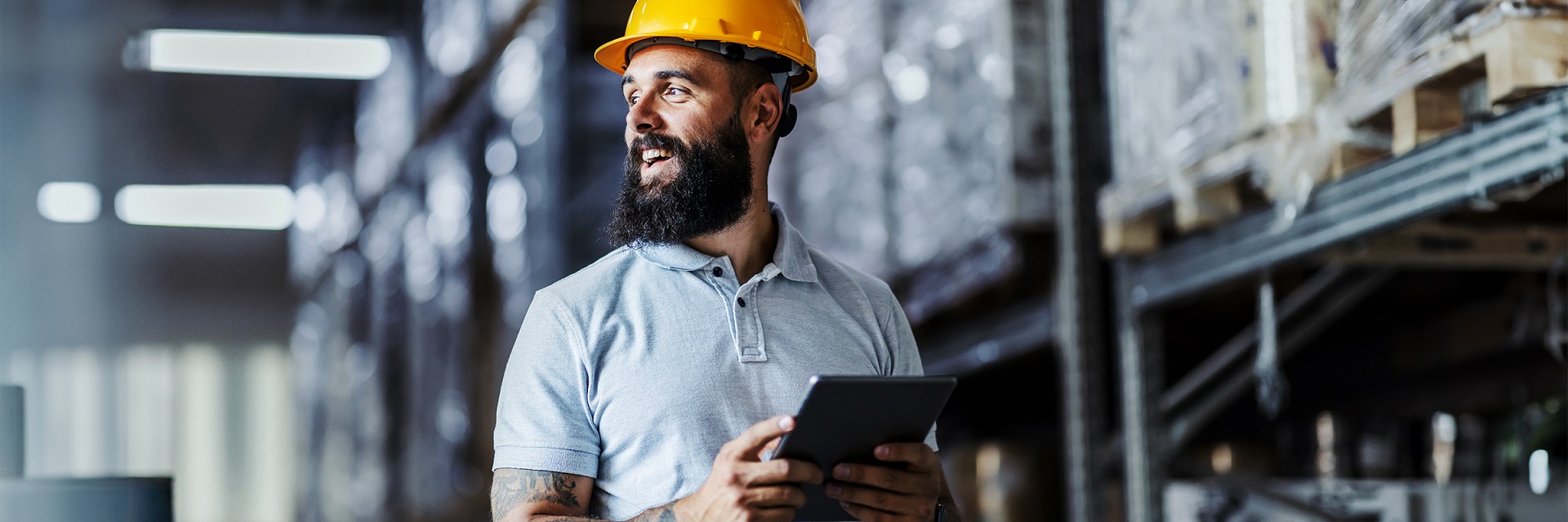 Ein Servicetechniker steht in einer Fabrikhalle mit Helm und Tablet