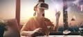 Eine Frau sitzt mit VR-Brille am Schreibtisch und interagiert mit virtuellen Objekten
